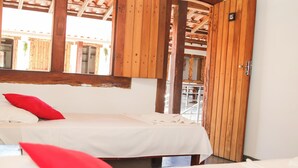 A room with two beds, each with a white bedspread and red pillows. There is a wooden door with a number plate, and the room has a wooden ceiling. - POUSADA LUZ DO SOL (Porto Seguro)