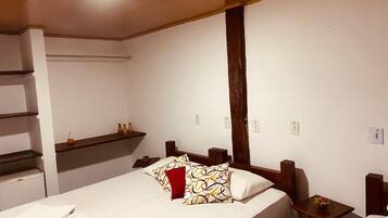 A bedroom with a bed, a nightstand, a wooden headboard, a shelf, and a wall-mounted light.