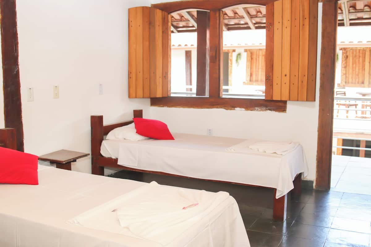A room with two beds, wooden beams, and a window with wooden shutters.