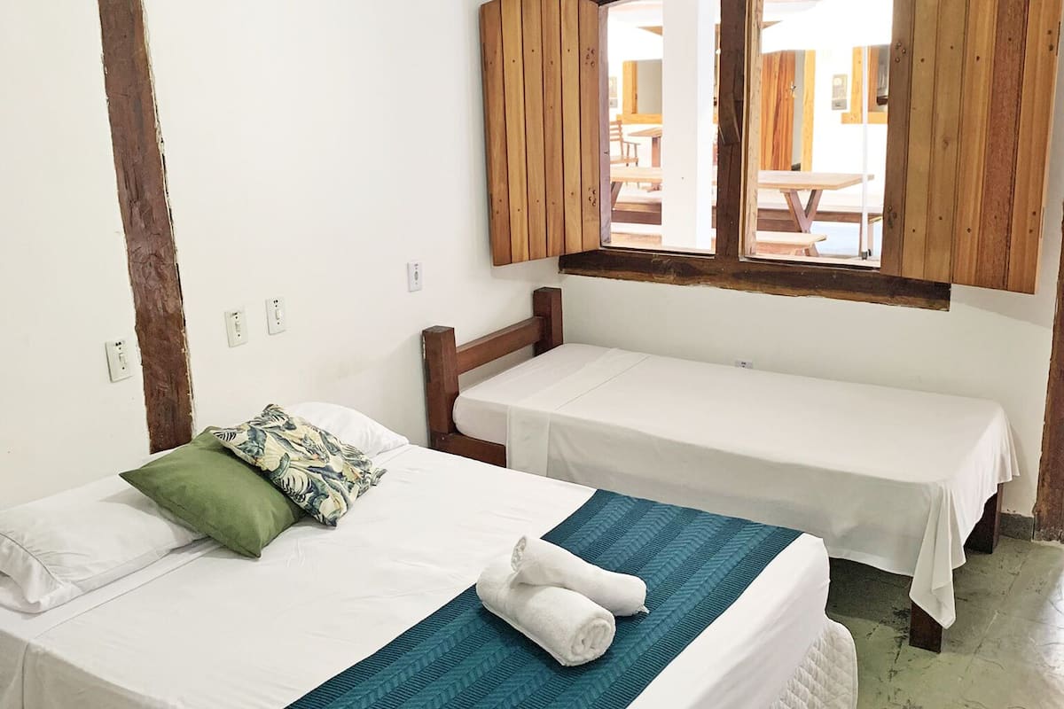 A room with two single beds, a wooden headboard, a window with wooden shutters, and a small table.