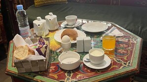 A breakfast setup on a colorful table with a view of a balcony and a window. - Hotel Transatlantique (Tunis)