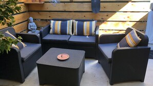 A patio area with wicker furniture, a Buddha statue, and a wooden fence. - Joli Petit Mazet Avec Terrasse en Pleine Nature (COGOLIN)