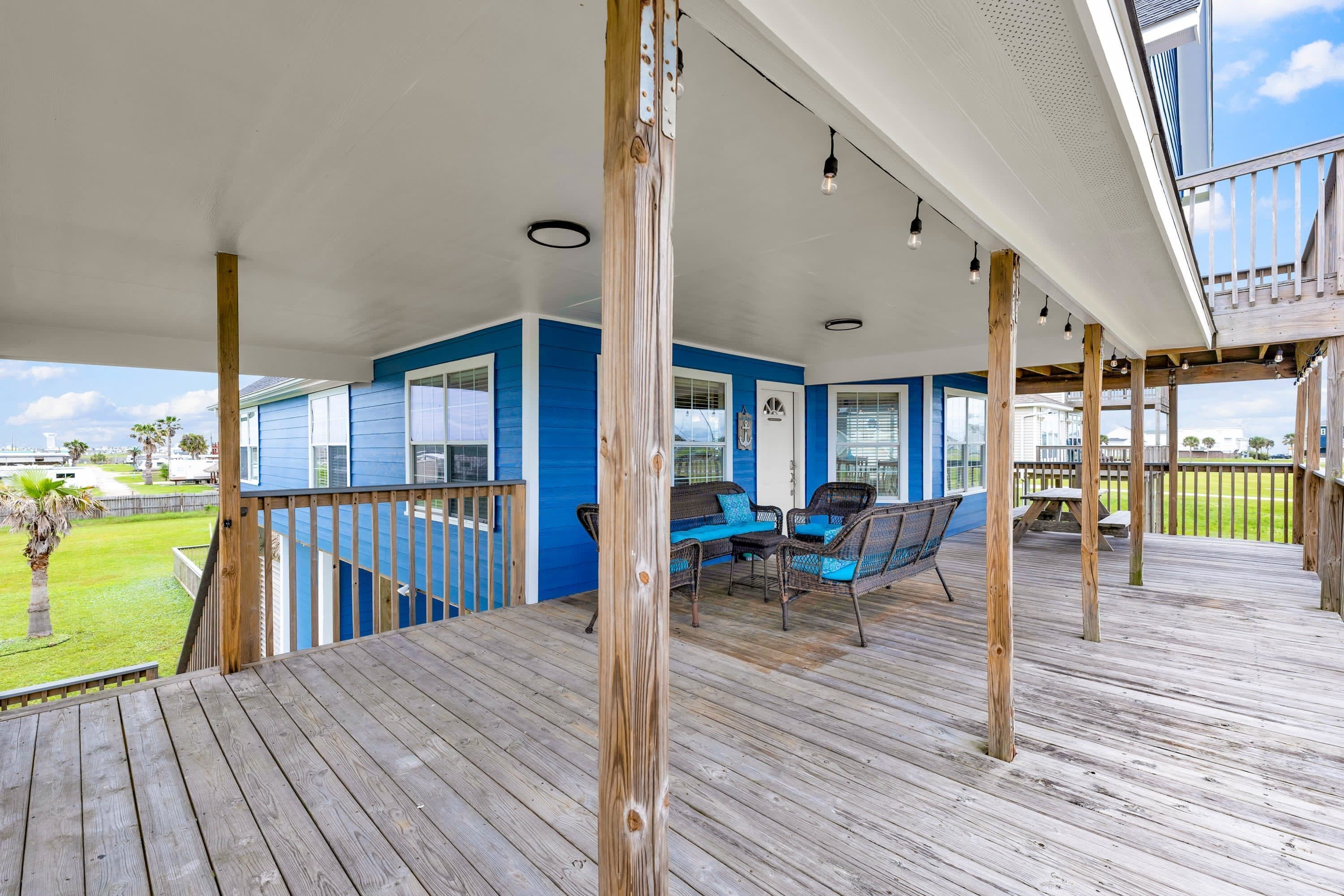 A covered outdoor area with a wooden deck, blue walls, and a seating area with chairs and a table.