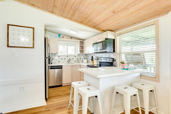 A modern kitchen with white cabinetry, a central island with stools, a stainless steel refrigerator, and a microwave.