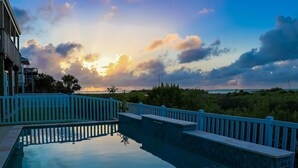A swimming pool with a blue railing, surrounded by greenery and a view of the ocean.