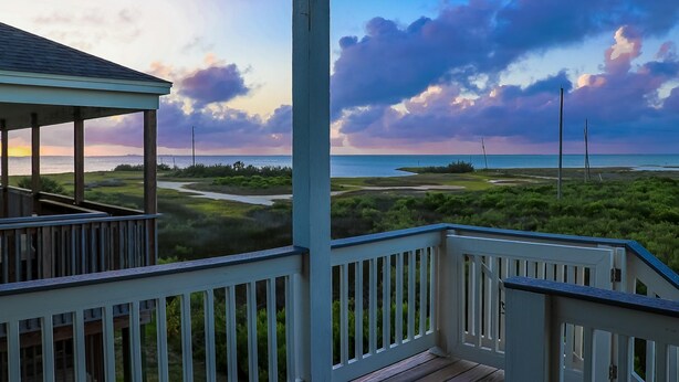A covered deck with a view of a coastal landscape, including a beach and grassy areas.