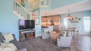 A spacious living room with a television, seating area, and a staircase leading to an upper level.