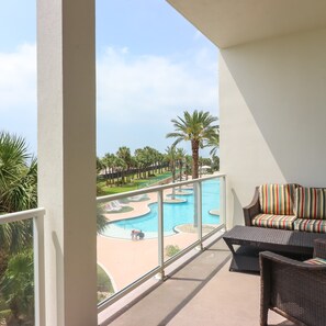 A balcony with a view of a swimming pool, surrounded by palm trees and lounge chairs.