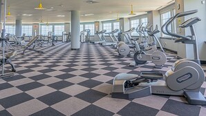 A gym with various exercise machines, a checkered floor, and large windows. - Beachfront Laid Back and Luxurious Diamond Beach Condo (Galveston)