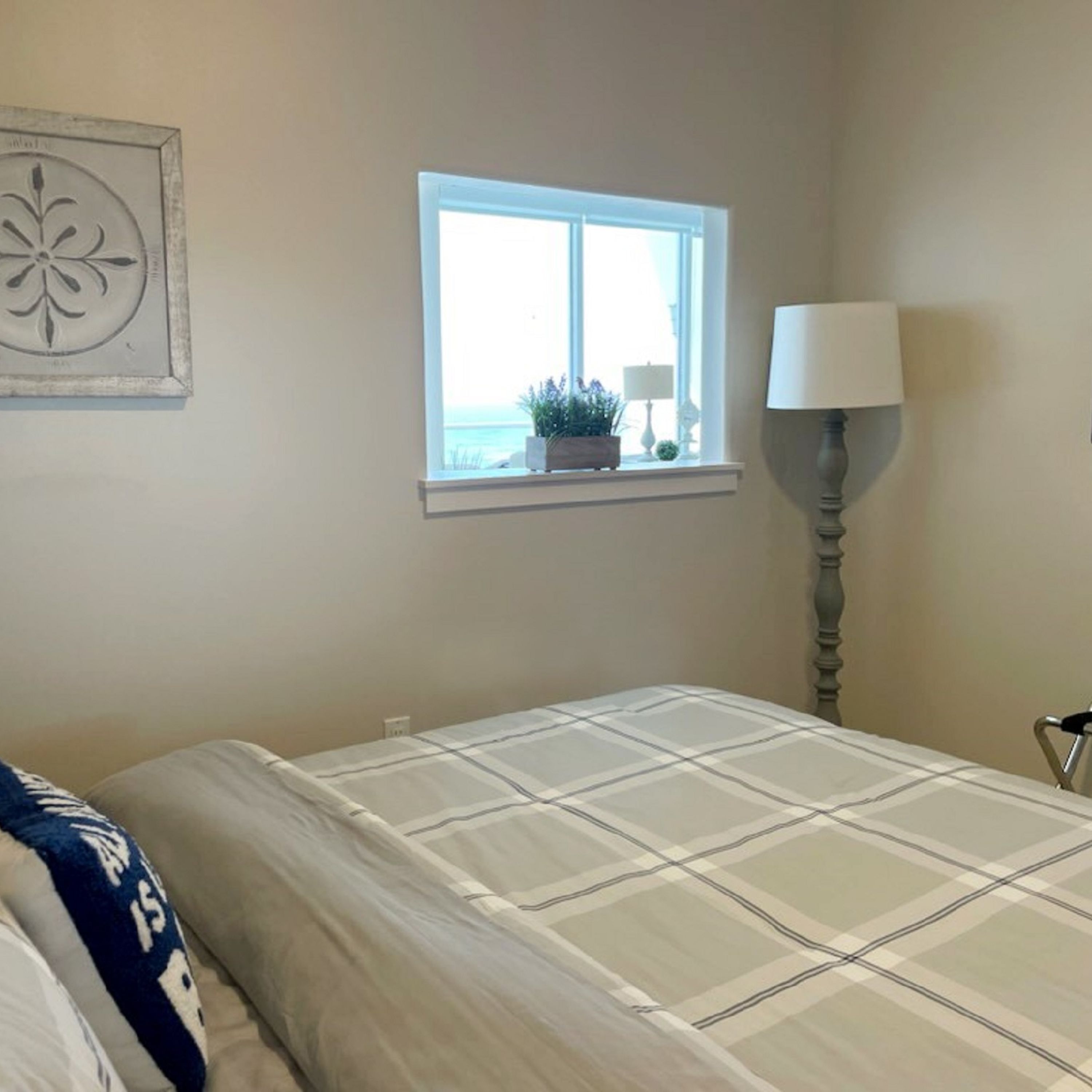 A bedroom with a bed, a window with a view, a bedside lamp, and a wall decoration.
