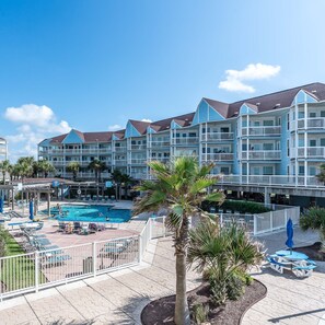 A multi-story hotel with a swimming pool, outdoor seating, and palm trees.