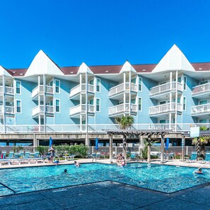 A hotel with multiple balconies, a swimming pool, and outdoor seating areas.