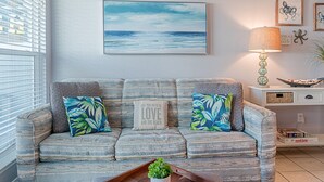 Un salon avec un canapé, un tableau représentant une plage, une lampe et un plateau sur lequel se trouve une plante.