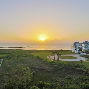 A beachfront property with a large building, a golf course, and a sunset view.