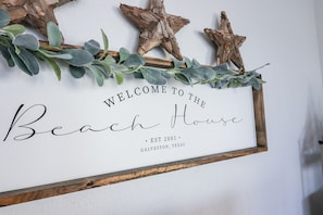 A welcome sign for 'Beach House' with a rustic design, including wooden stars and eucalyptus leaves.