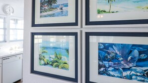 Quatre tableaux encadrés sont accrochés au mur, représentant des scènes tropicales avec des palmiers et de l’eau.