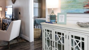 A well-lit living room with a TV, a comfortable chair, a cabinet with decorative items, and a painting on the wall.