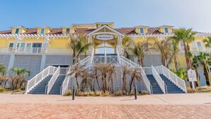 A beachfront hotel with a central entrance, multiple balconies, and a sign indicating a beach club.