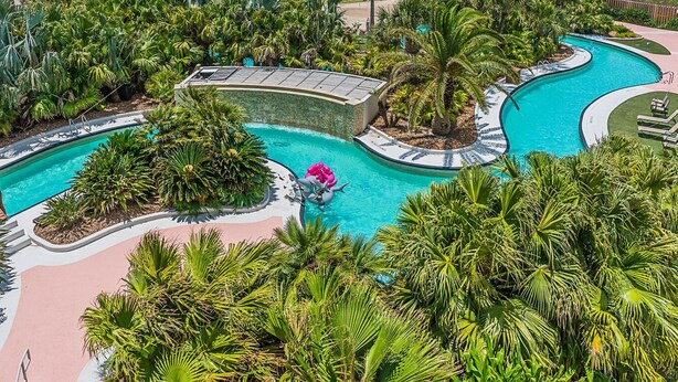A resort with a large pool area, palm trees, and a view of the ocean. - Seas the Day in This Luxury Condo at Diamond Beach Ocean Views Incredible Pools Amenities (Galveston)