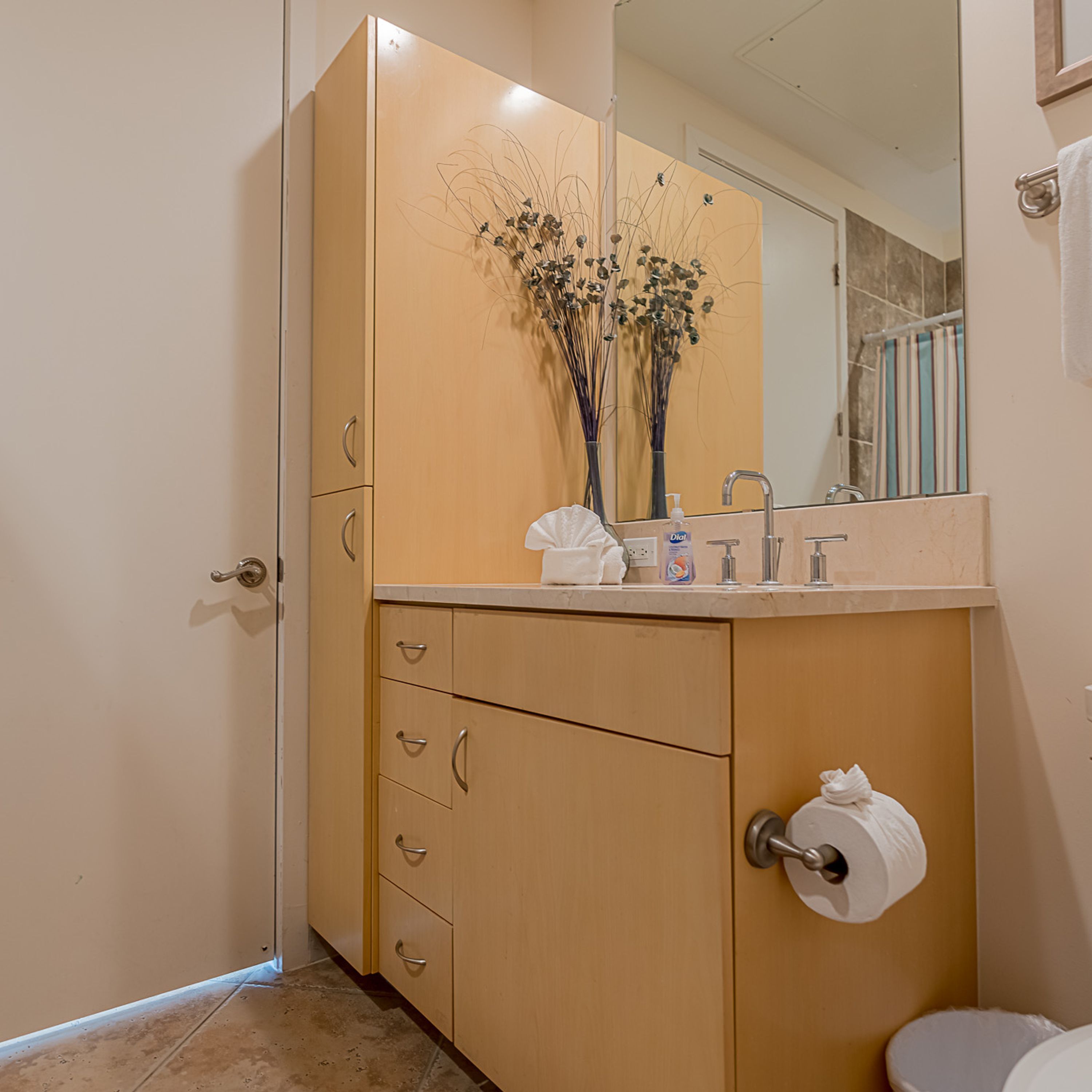 A bathroom with a beige cabinet, a mirror, a toilet, and a sink with a soap dispenser.