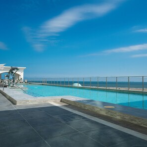 A swimming pool with a view of the ocean, a lifeguard stand, and a clear sky.