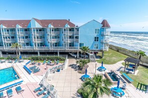 A beachfront hotel with multiple balconies, a swimming pool, and outdoor seating areas. - Steps to Pool and Beach Amazing Views From Two Balconies (Galveston)