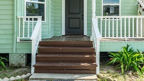 A green house with a front door, a porch, and a staircase leading to a second-story balcony. - Adventure Awaits Close to the Beach (Galveston)