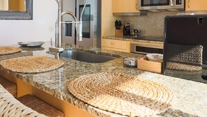 A modern kitchen with granite countertops, stainless steel appliances, and woven placemats. - Western Waves Dreamy Diamond Beach Condo - Mind-blowing Views Amenities (Galveston)