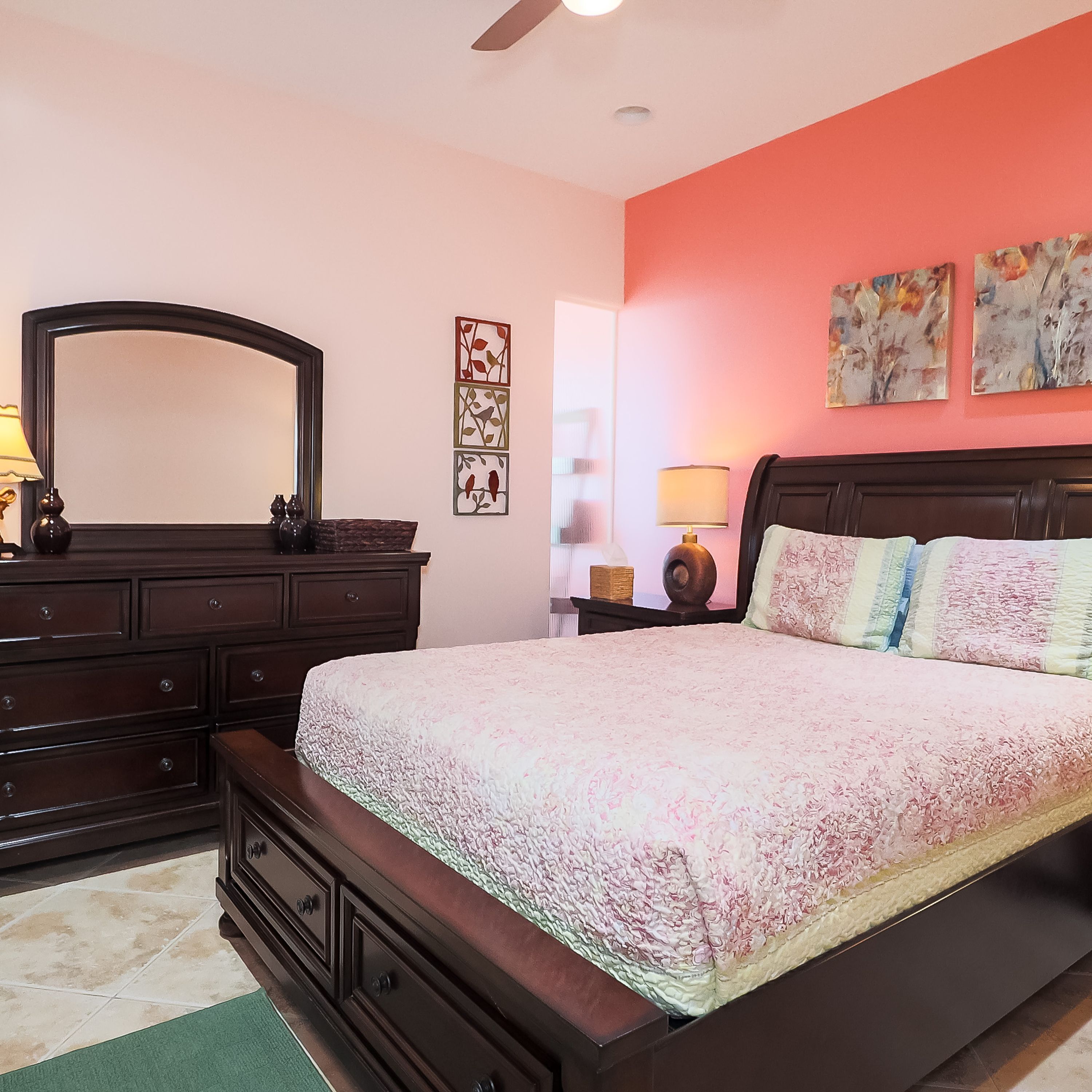 A bedroom with a large bed, a dresser, a mirror, and artwork on the walls.