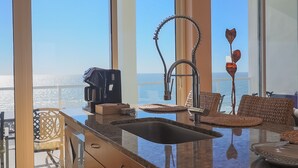 A modern kitchen with a large island, a coffee maker, and a view of the ocean. - Western Waves Dreamy Diamond Beach Condo - Mind-blowing Views Amenities (Galveston)