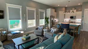 A modern living room with a teal sofa, a coffee table, and a ceiling fan. - Beachside Paradise Retreat With Luxury (Galveston)