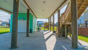 A covered outdoor area with wooden beams and a concrete floor, leading to a garage and a green building. - The Coast is Clear Great Home By Beach Bay (Galveston)