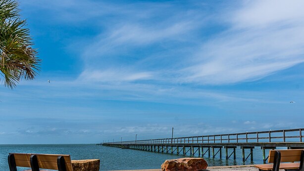 A beach with benches, large rocks, and a pier extending into the water. - The Coast is Clear Great Home By Beach Bay (Galveston)