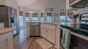 A modern kitchen with white cabinets, stainless steel appliances, and a wooden floor. - The Coast is Clear Great Home By Beach Bay (Galveston)