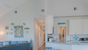 A modern kitchen with white cabinets, a central island with stools, and a blue accent wall. - The Coast is Clear Great Home By Beach Bay (Galveston)
