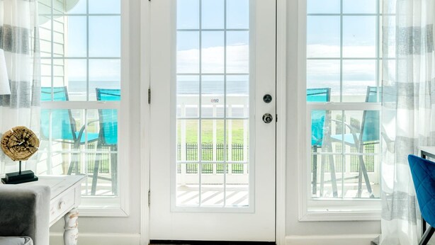 A room with a white door, two windows, and a view of the outdoors.