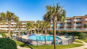 A hotel with a central swimming pool surrounded by palm trees and lounge chairs.