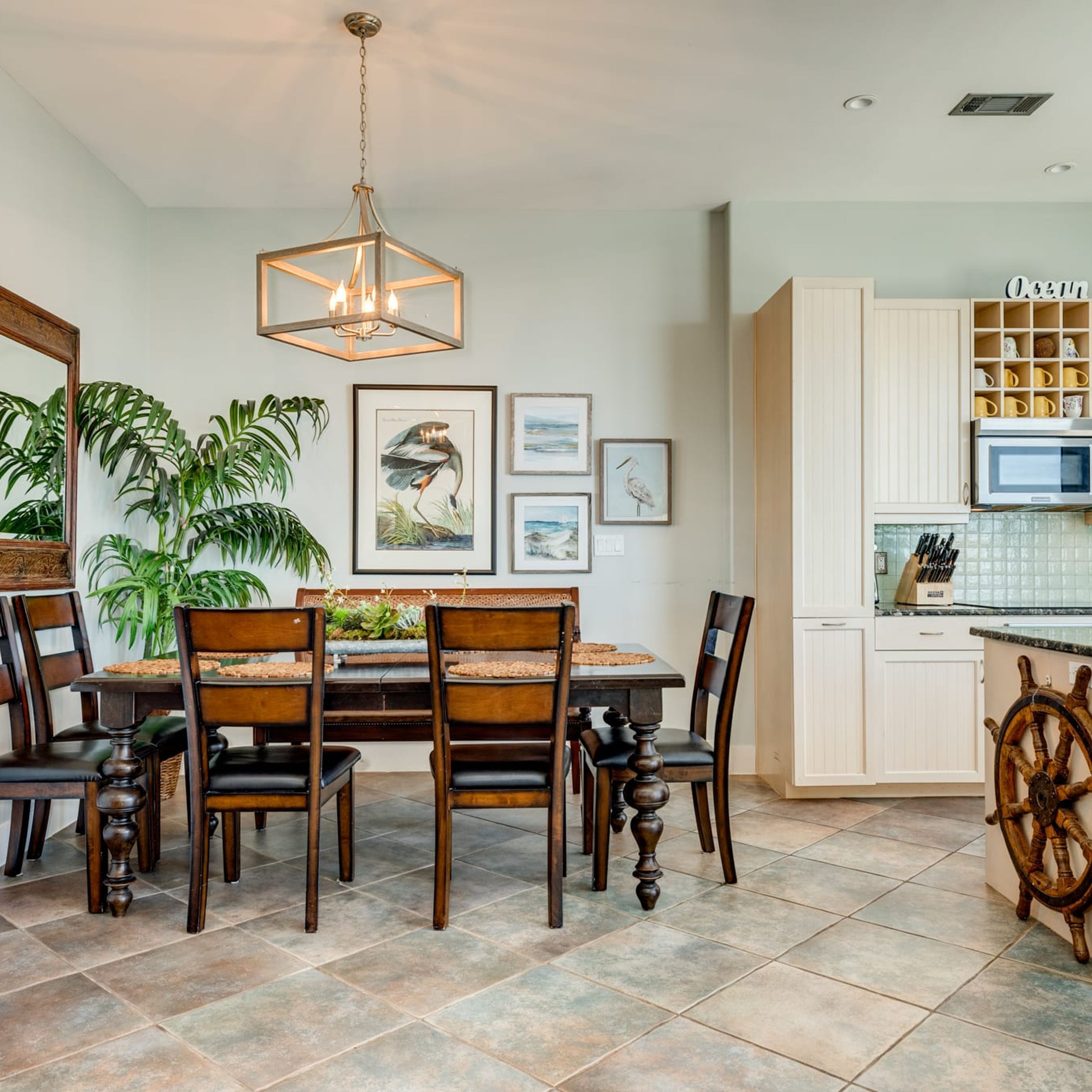 A dining area with a wooden table and chairs, surrounded by framed artwork and potted plants.
