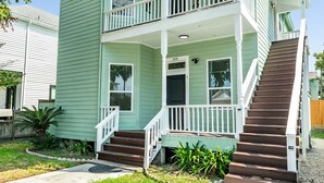A two-story house with a front porch, a staircase, and a small garden area. - Have fun Relax and Stay Close to the Beach (Galveston)