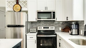 A modern kitchen with white cabinets, stainless steel appliances, a microwave, a toaster, and a coffee maker. - Have fun Relax and Stay Close to the Beach (Galveston)