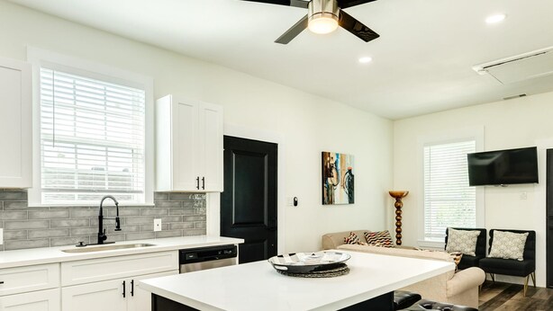 A modern kitchen with white cabinets, a black countertop, and a central island with bar stools. - Have fun Relax and Stay Close to the Beach (Galveston)