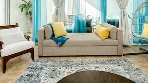 A modern living room with a beige sofa, two yellow cushions, a wooden chair, and a blue patterned rug. - Warm and Welcoming Views at Diamond Beach (Galveston)
