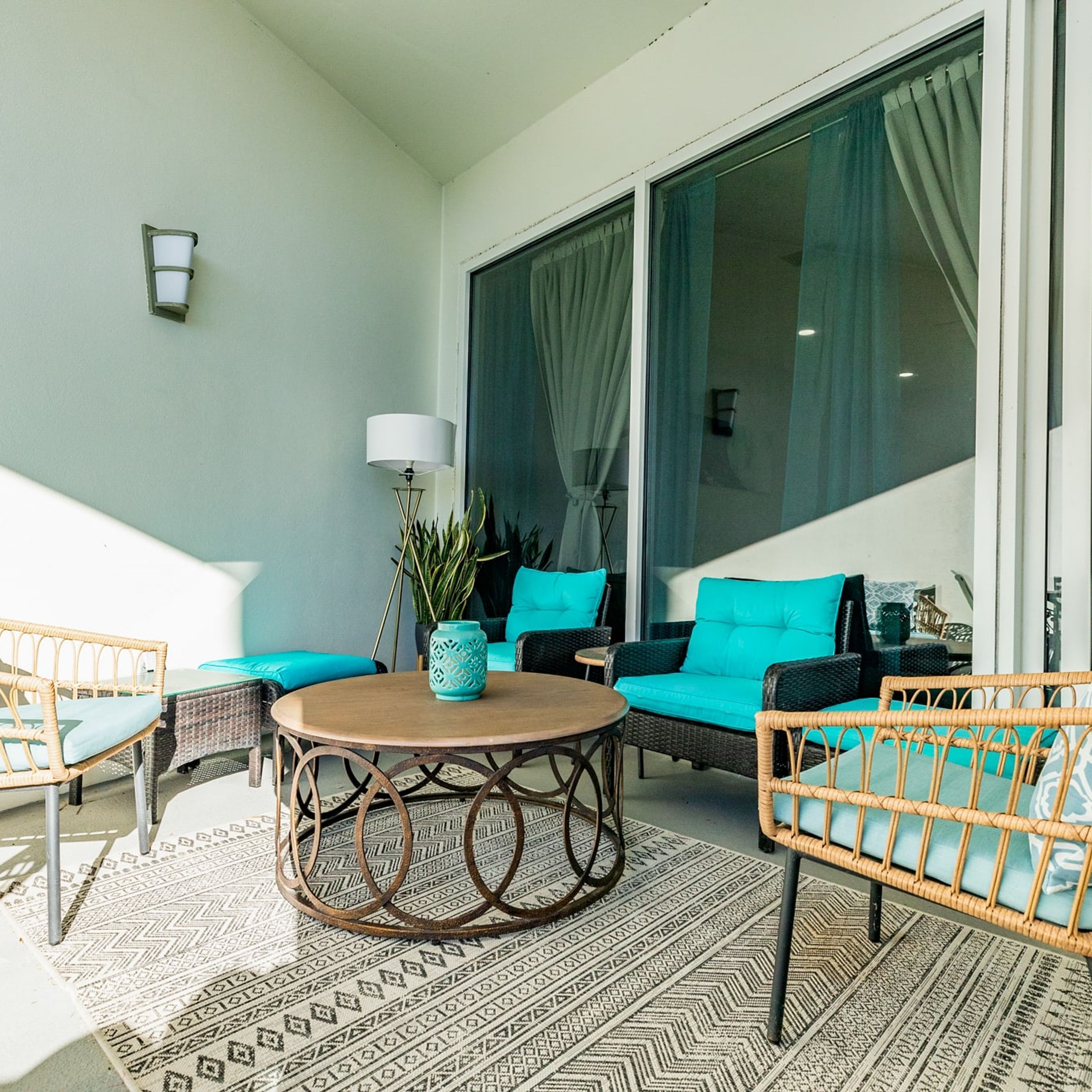 A sunlit outdoor seating area with wicker furniture, a round table, and a potted plant.