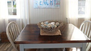 A dining area with a wooden table, a bowl of decorative stones, and a wall with a 'FEELIN BEACHY' sign. - In-home Bar Lounge and Arcade Stay Entertained at The Sea Shed (Galveston)
