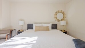 Une chambre d’hôtel avec un grand lit, deux tables de chevet avec des lampes, un miroir rond et un petit bureau avec une chaise.