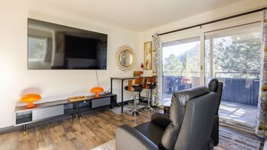 Un salon comprenant un canapé, un téléviseur, une table basse et un coin repas avec des chaises.