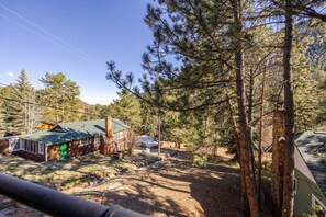 Una cabaña con techo verde, rodeada de altos pinos y un cielo despejado.