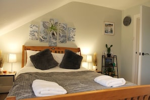 Een netjes opgemaakt bed met twee kussens, een bedlampje en een lijst met een afbeelding aan de muur.