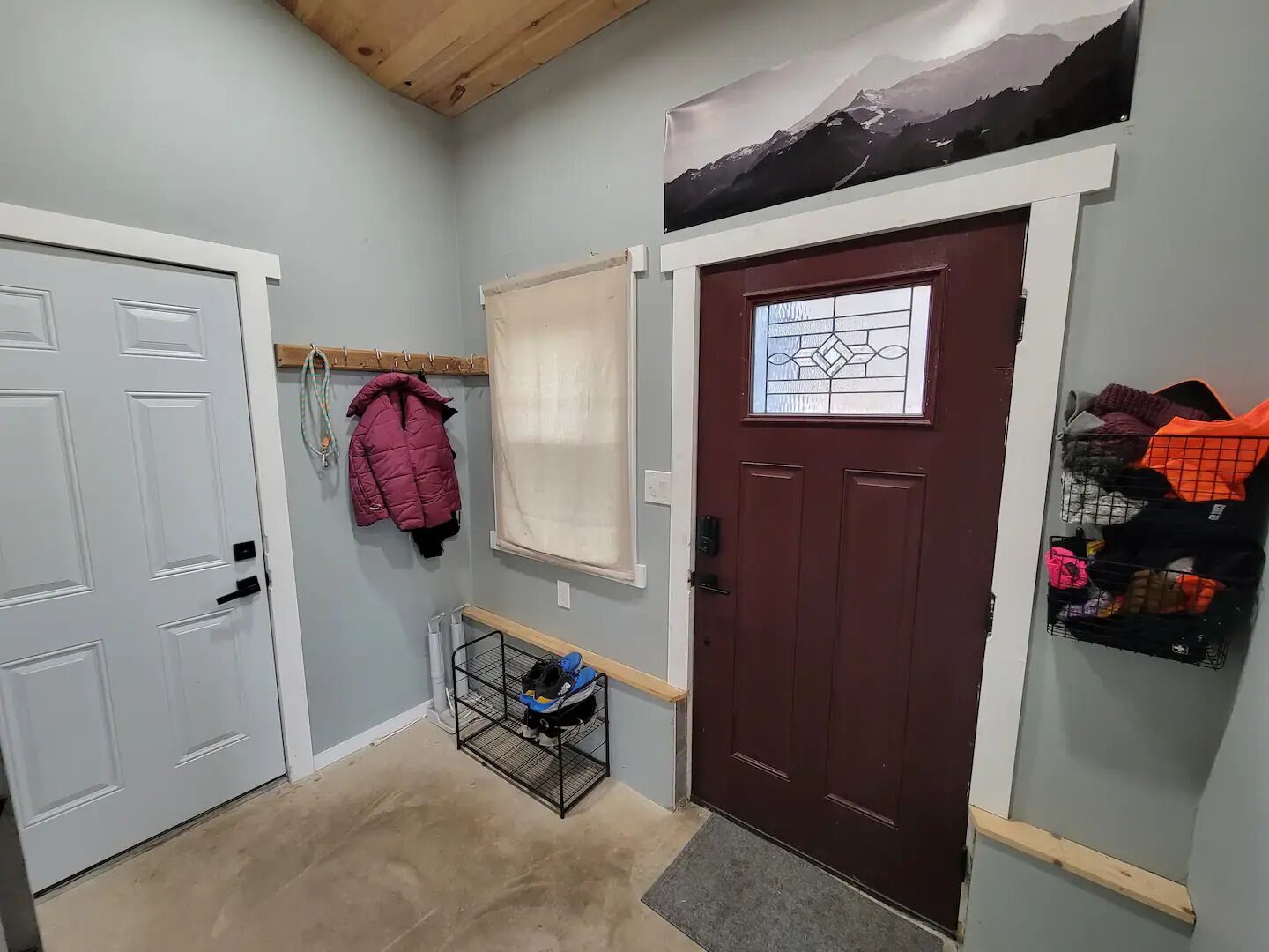 A hallway with a white door, a maroon door with a stained glass window, and a coat rack with a red jacket.