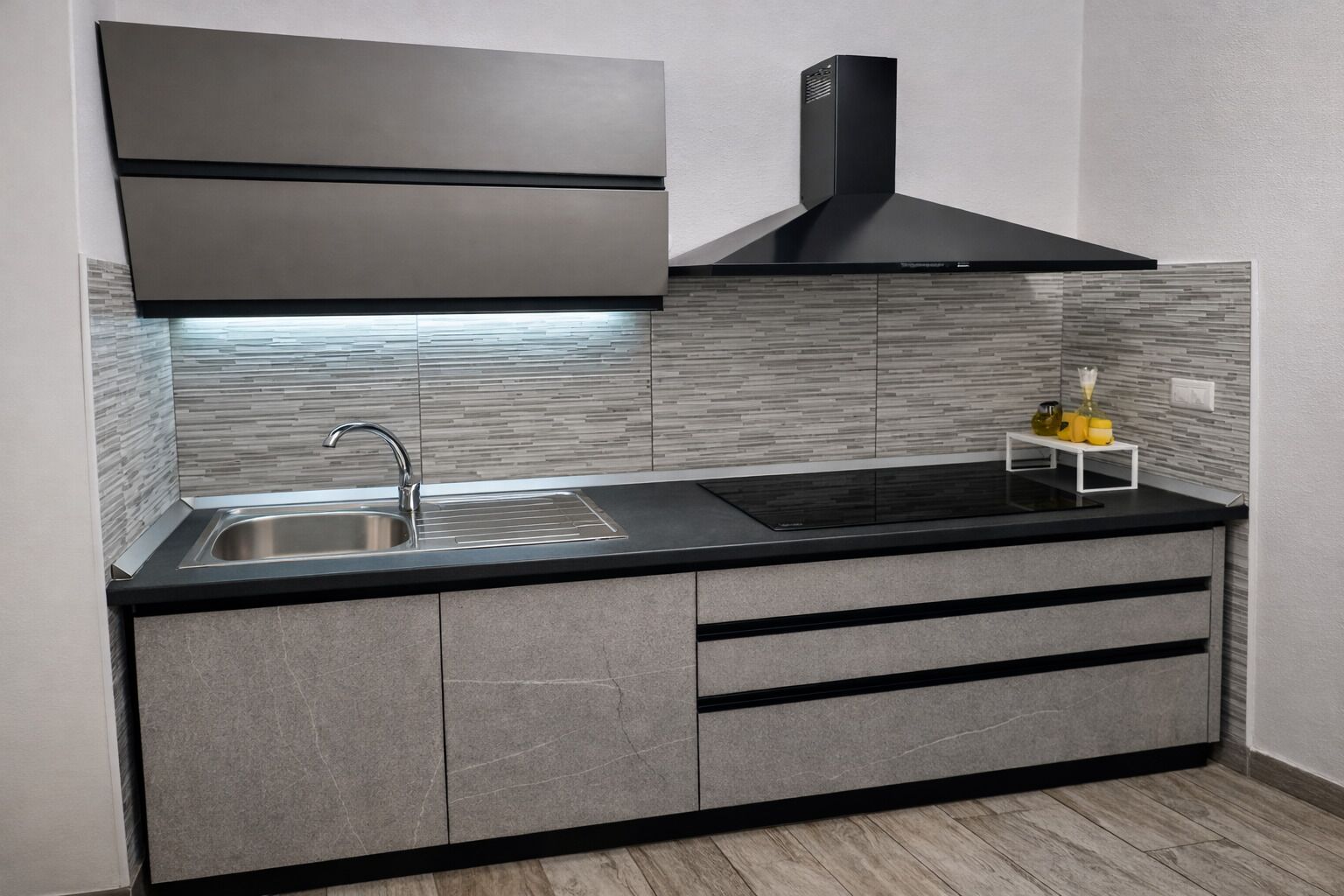 A modern kitchen with a stainless steel sink, black countertop, and grey cabinetry.